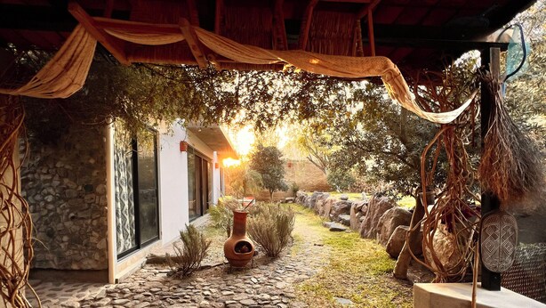 A stone pathway leading to a rustic outdoor area with a thatched roof, a decorative vase, and a bamboo stick. - Casa Tacuba country house near the mountain and lake Chapala (San Juan Cosalá)