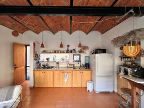 A kitchen with wooden cabinets, a refrigerator, a stove, and hanging pendant lights.