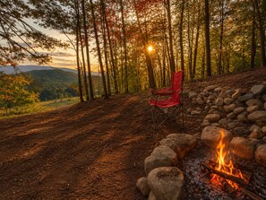 A forested area with a fire pit and a red chair.