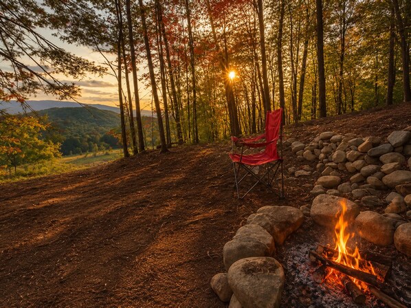 A forested area with a fire pit and a red chair.