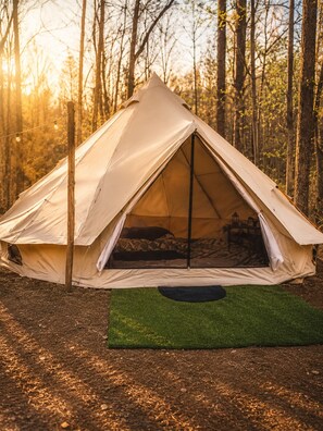 A tent with a simple design, set up in a forest with trees in the background.