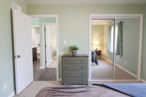 A bedroom with a bed, a dresser, a mirror, and a door leading to a bathroom.