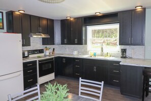 A modern kitchen with dark cabinets, a white refrigerator, and a window providing a view of the outdoors.