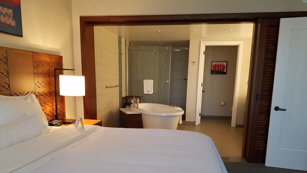 Habitación de hotel con una cama grande, una lámpara de noche, un baño con bañera y ducha.