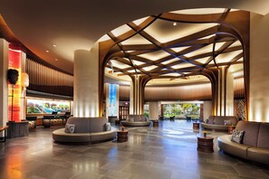 Um hall amplo com design moderno, apresentando uma área de estar central com sofás e uma estrutura de teto curva.