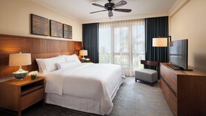 Habitación de hotel con una cama grande, televisor de pantalla plana, escritorio con lámpara y ventilador de techo.