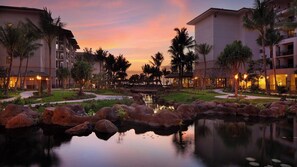 Um resort com piscina, palmeiras e um pôr do sol.