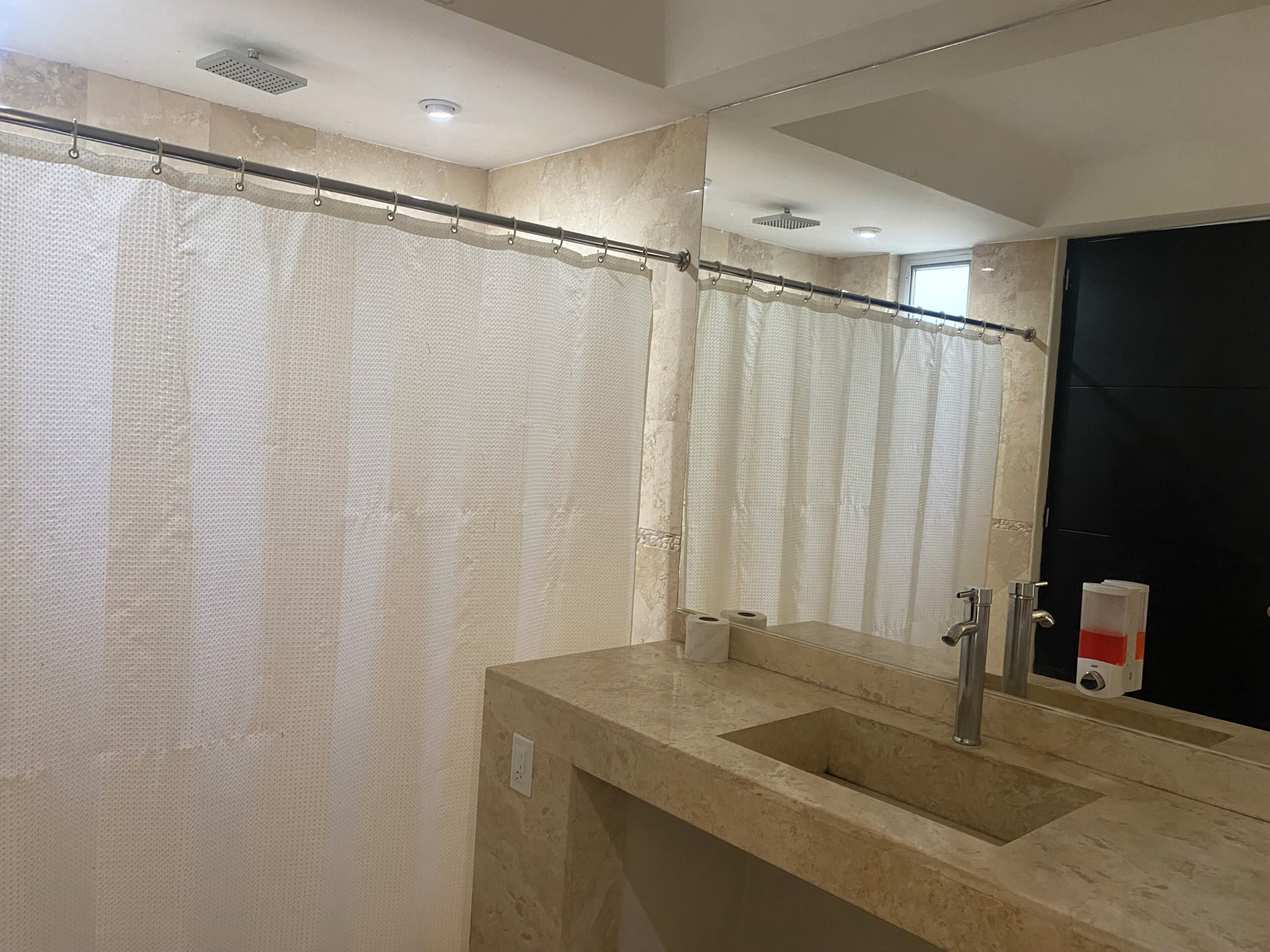 Une salle de bain avec un rideau de douche, un lavabo, un miroir et une porte noire.