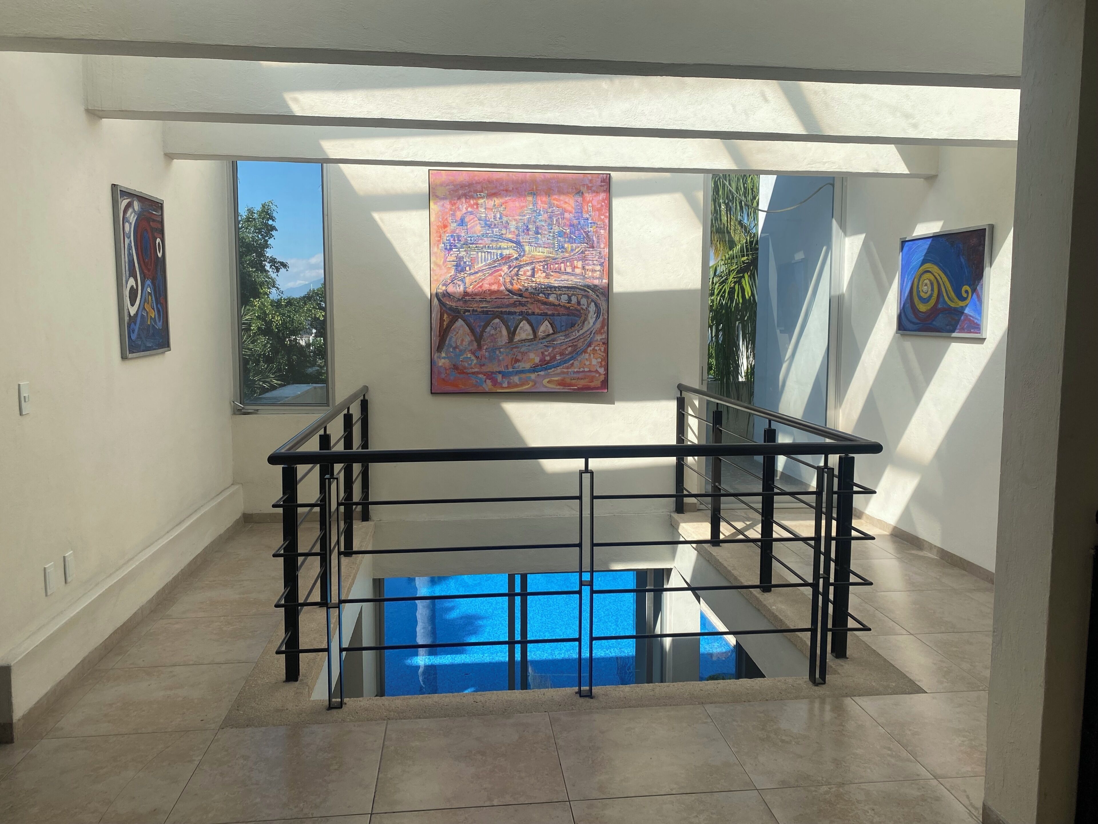 A modern interior with a staircase leading to a lower level, a glass pool, and artwork on the walls.