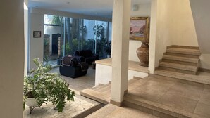 Ein modernes Interieur mit einer Treppe, einer Sitzecke mit Sofa und Sesseln und einem großen Fenster mit Blick ins Freie.