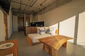 Un dormitorio moderno con una cama de madera, un escritorio pequeño y una kitchenette al fondo.