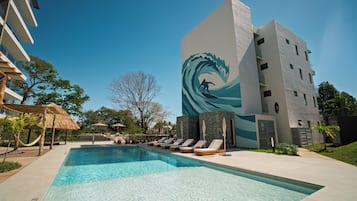 Una piscina con sillones de descanso, un mural de un surfista y un edificio de diseño moderno.