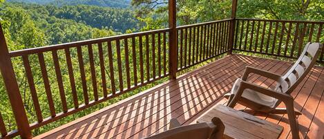 A wooden deck with a view of a forested valley and mountains.