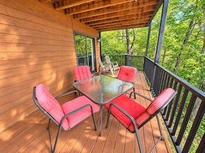A wooden deck with a glass table and red chairs, surrounded by a railing and trees. - Mountain Ridge-VIEWS-Pigeon Forge | Hot Tub, Decks & Fireplace | Sleeps 4 (Pigeon Forge)