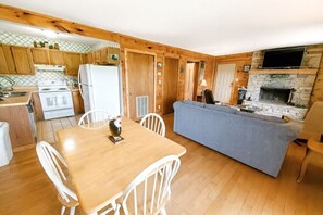 A compact kitchen with wooden cabinets, a white refrigerator, a stove, and a dining area with a table and chairs. - Mountain Ridge-VIEWS-Pigeon Forge | Hot Tub, Decks & Fireplace | Sleeps 4 (Pigeon Forge)