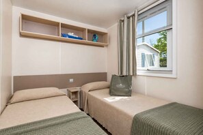 Une chambre d’hôtel avec deux lits simples, une petite table, une étagère avec un modèle de bateau et une fenêtre avec des rideaux.