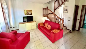 Ein Wohnzimmer mit einem roten Sofa, einem Fernseher auf einem Schrank, einer Treppe und einer Deckenleuchte.