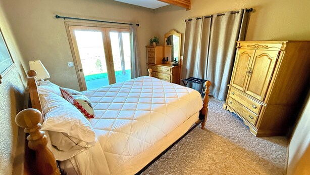 Une chambre à coucher avec un lit, une commode, un miroir et une fenêtre avec des rideaux.