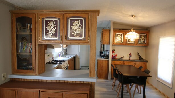 A kitchen with wooden cabinets, a dining table, chairs, and a pendant light. - 2 Bedroom, 2 Bath, Mobile Home, Great Location in Athens, Steps To Bike Path (Athens)