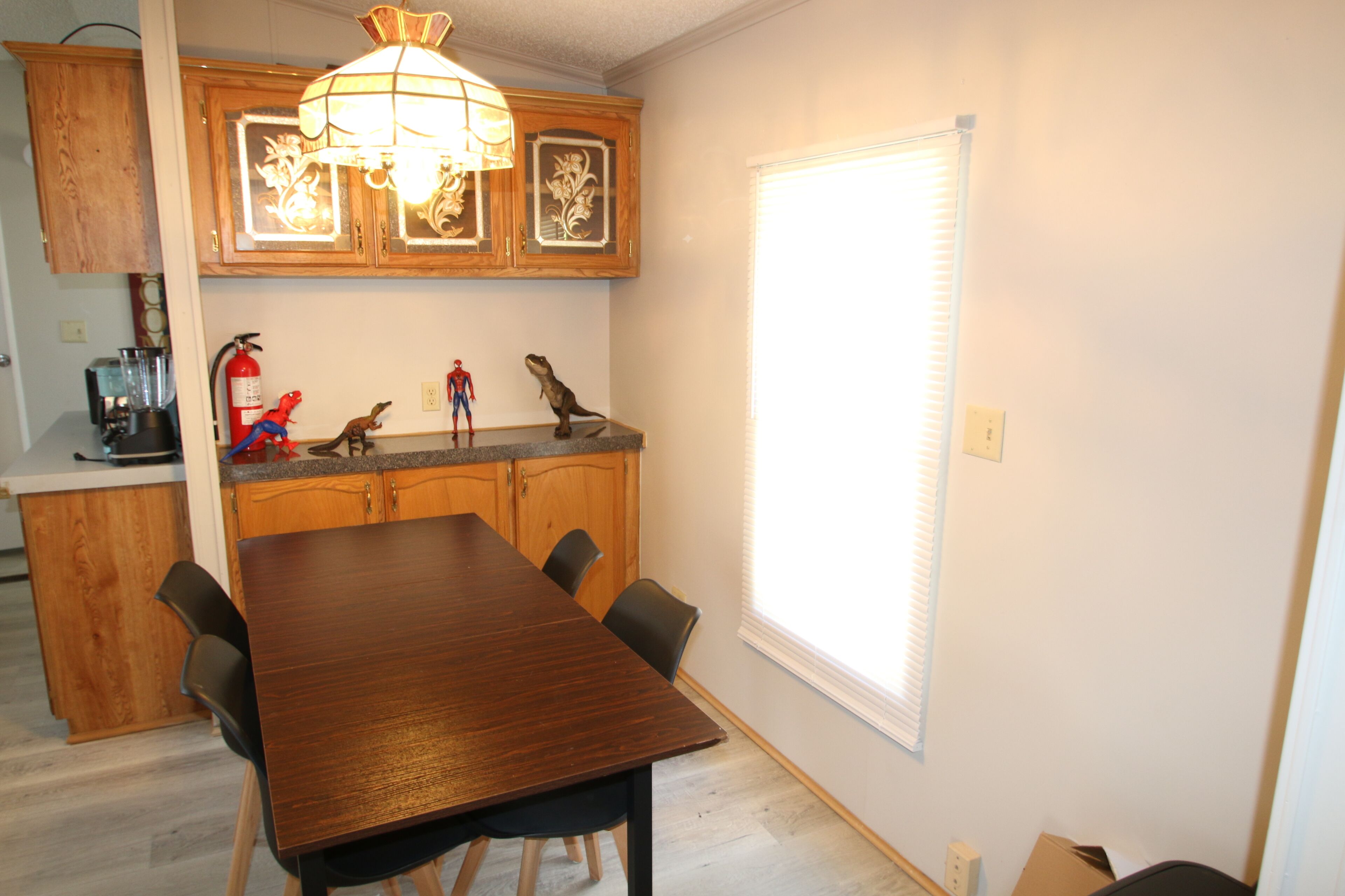 A dining area with a wooden table and chairs, a kitchen with wooden cabinets, and a window with blinds.
