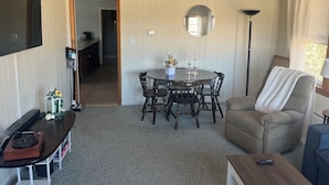 A dining area with a round table, chairs, a sofa, a TV, and a lamp.