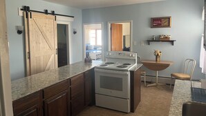 A kitchen with a stove, cabinets, a sliding door, and a dining area with a chair and table.