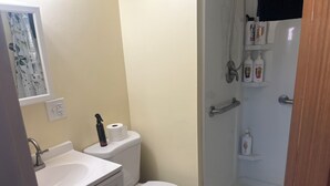 A bathroom with a toilet, sink, shower, and a shelf with toiletries.