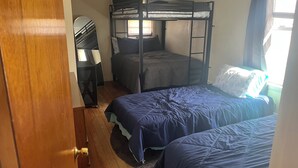 A bunk bed room with a wooden floor, a desk, and a window.
