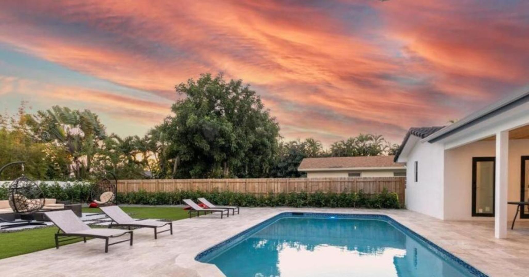 Une piscine avec des chaises longues, une clôture en bois et une maison en arrière-plan.