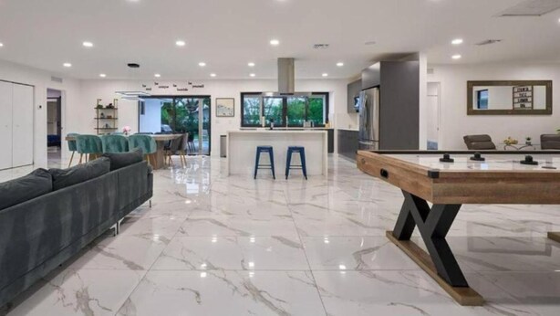 A modern living room with a pool table, a sofa, and a kitchen area in the background. - Peaceful Villa by Glam Homes (Hollywood)