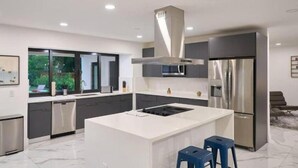 A modern kitchen with a central island, stainless steel appliances, and a view of greenery outside. - Peaceful Villa by Glam Homes (Hollywood)