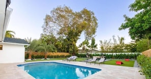 A swimming pool with lounge chairs, a grassy lawn, and trees.