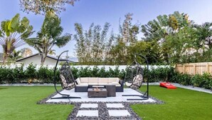 A patio with a sofa, two hanging chairs, and a fire pit. - Peaceful Villa by Glam Homes (Hollywood)