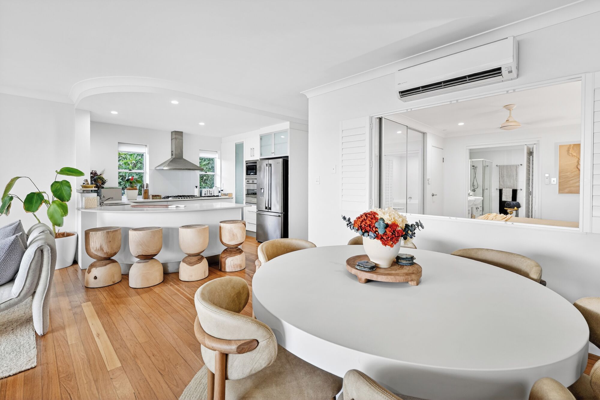 Een moderne keuken met een centraal eiland, een eetgedeelte met ronde tafels, en een grote spiegel die de ruimte weerspiegelt.