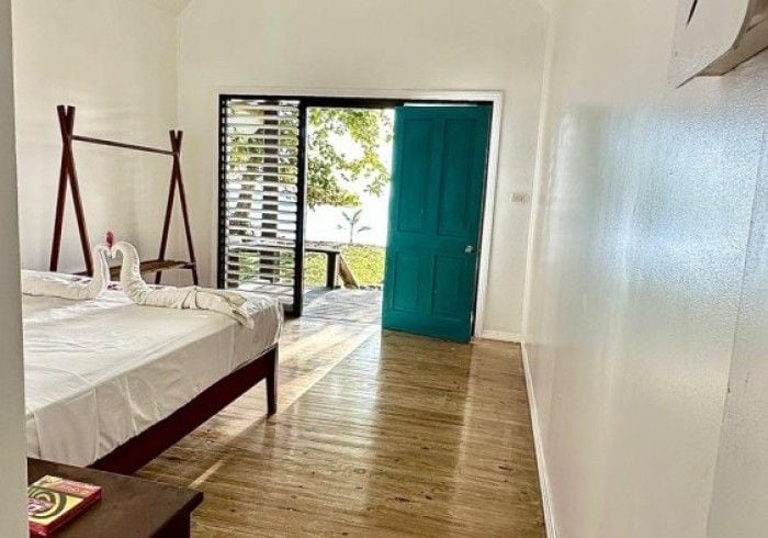 A bedroom with a bed, a wooden floor, a green door, and a view through a window.