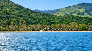 A coastal scene with a clear blue sea, a sandy beach, and a line of huts. - Koro Island Resorts Fiji (Koro Island)