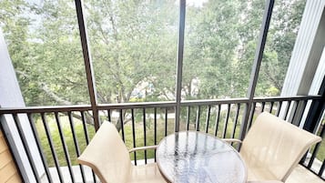 Un balcón con una mesa de vidrio y dos sillas, con vistas a un paisaje verde con árboles.