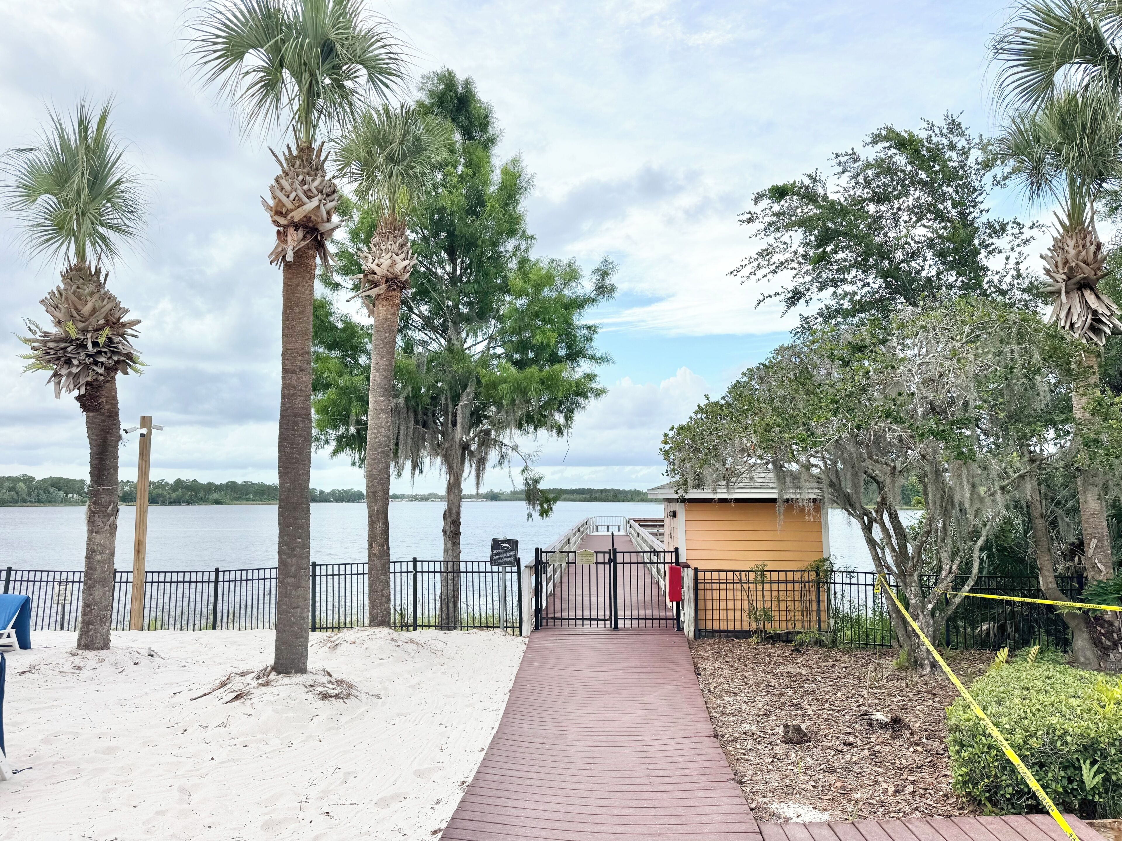 A pathway leading to a beach area with palm trees, a wooden structure, and a view of the water.