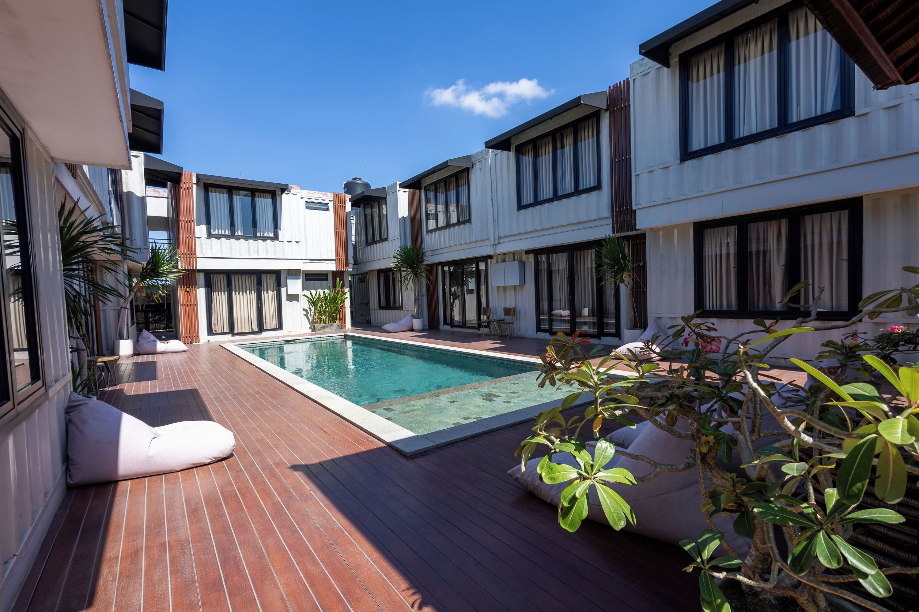 A modern residential building with a swimming pool, wooden deck, and potted plants.