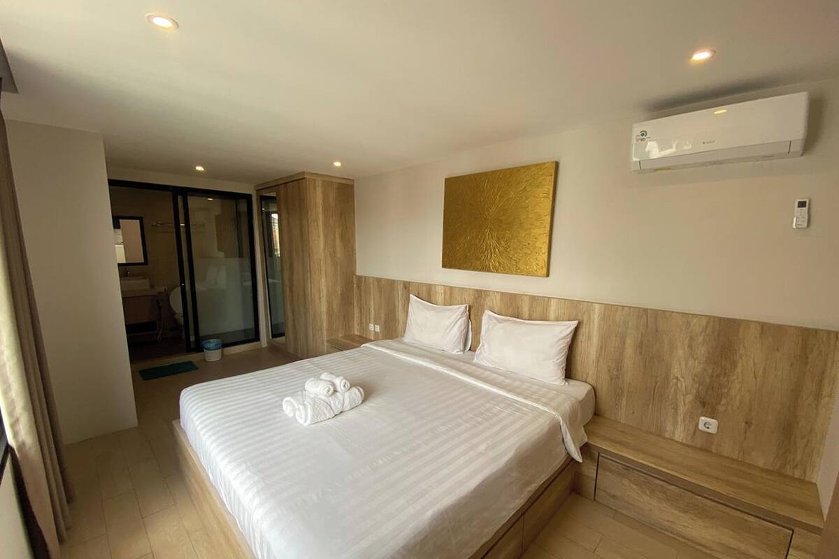 A hotel room with a large bed, a sliding door to a balcony, and an air conditioning unit on the wall.