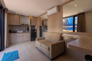 A compact kitchen with built-in appliances, a sofa, and a window with curtains. - Allende Canggu (Canggu)