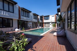 A modern pool area with a rectangular pool, wooden deck, and seating areas. - Allende Canggu (Canggu)