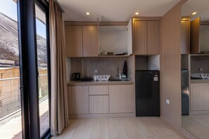 A modern kitchen with wooden cabinets, a black refrigerator, and a window with curtains. - Allende Canggu (Canggu)