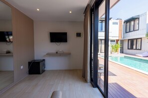 Een moderne woonkamer met een flatscreen televisie aan de muur, een klein tafeltje met een zakdoosje en een zwarte draagbare verwarming op de vloer.