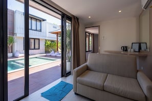 A modern living room with a sofa, a coffee table, and a view of an outdoor swimming pool. - Allende Canggu (Canggu)