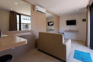 A hotel room with a sofa, a TV mounted on the wall, a flat-screen TV, a small table, and a window with curtains. - Allende Canggu (Canggu)