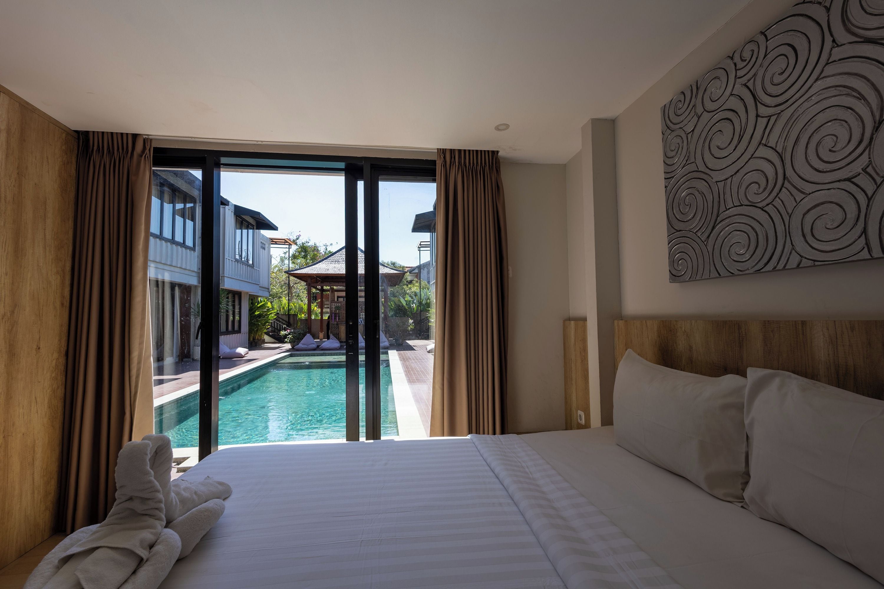 A hotel room with a bed, a view of a swimming pool, and a large window with curtains.