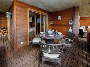 Eine Holzterrasse mit einem runden Glastisch, Korbstühlen und einem Essbereich mit Tisch für zwei Personen.