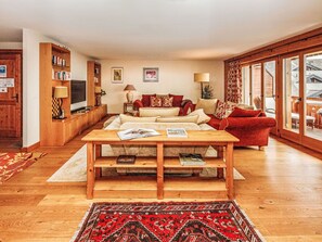 A living room with a wooden coffee table, red sofa, and a large window with a view of a house. - Lovely apartment for 6 people with WIFI, TV and balcony (Ollon)