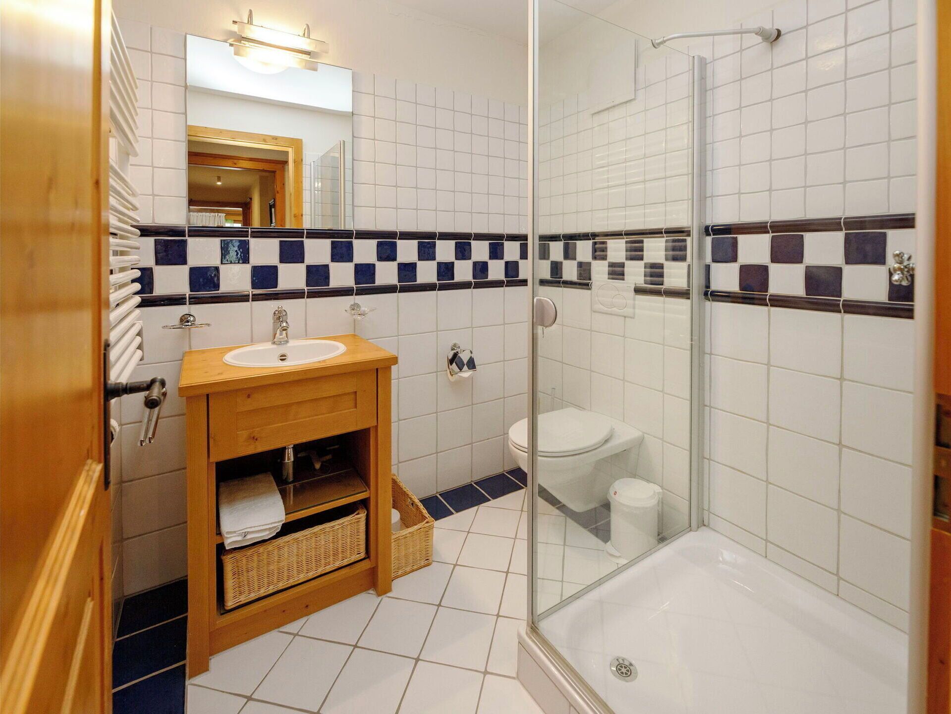 Une salle de bain avec un meuble-lavabo en bois, un lavabo blanc, des toilettes et une douche séparée par une paroi de verre.